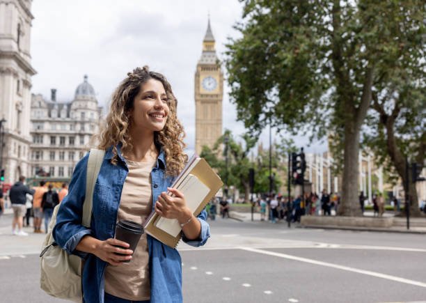 Portrait of a happy exchange student walking outdoors in London and drinking coffee on-the-go